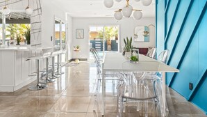 A modern kitchen with a long dining table, clear chairs, and a blue accent wall.