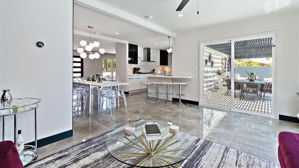 A modern kitchen with a central island, bar stools, and a dining area with a glass table.