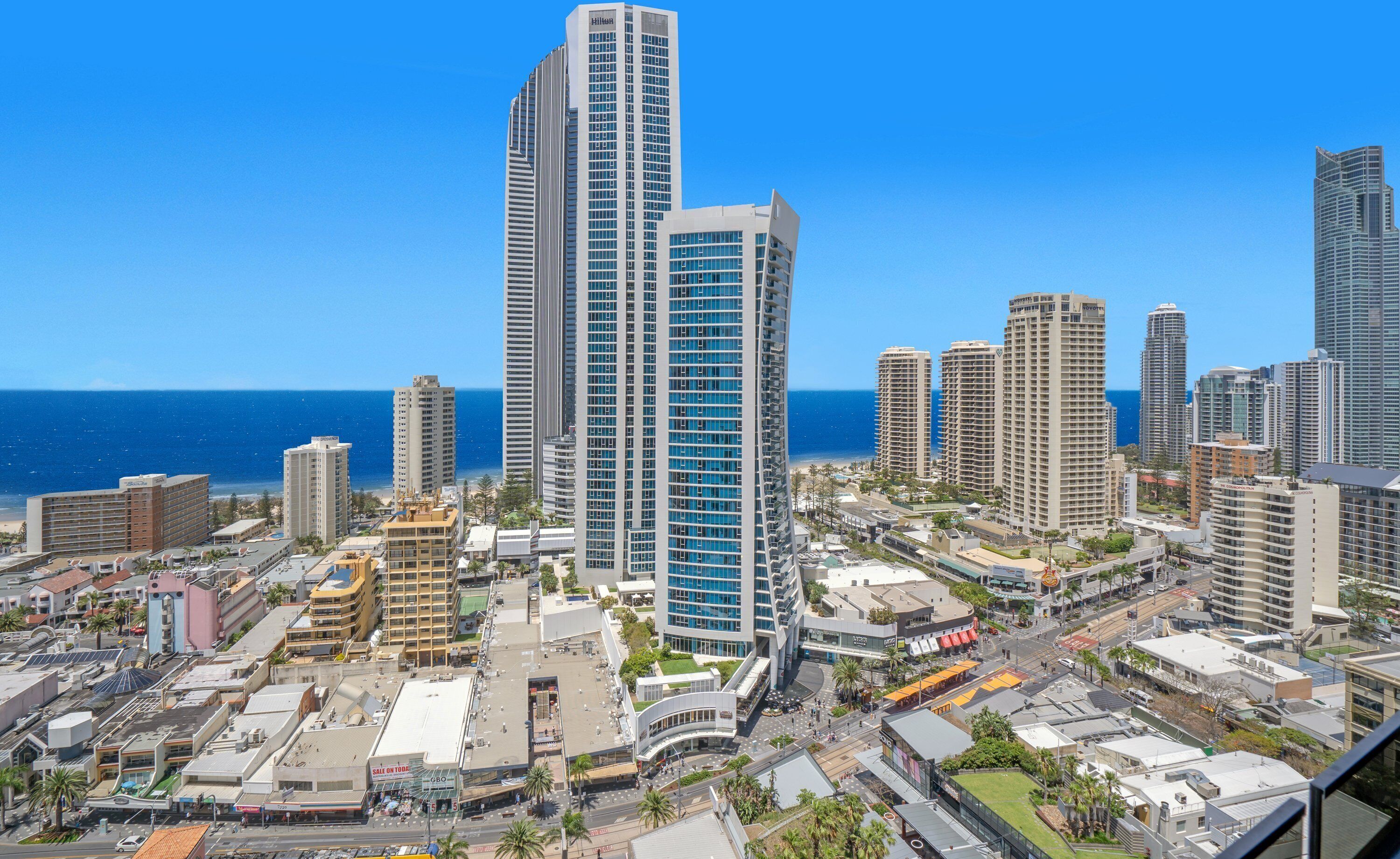Hotel moderno com arquitetura imponente, situado em uma paisagem urbana costeira com vista para o oceano.