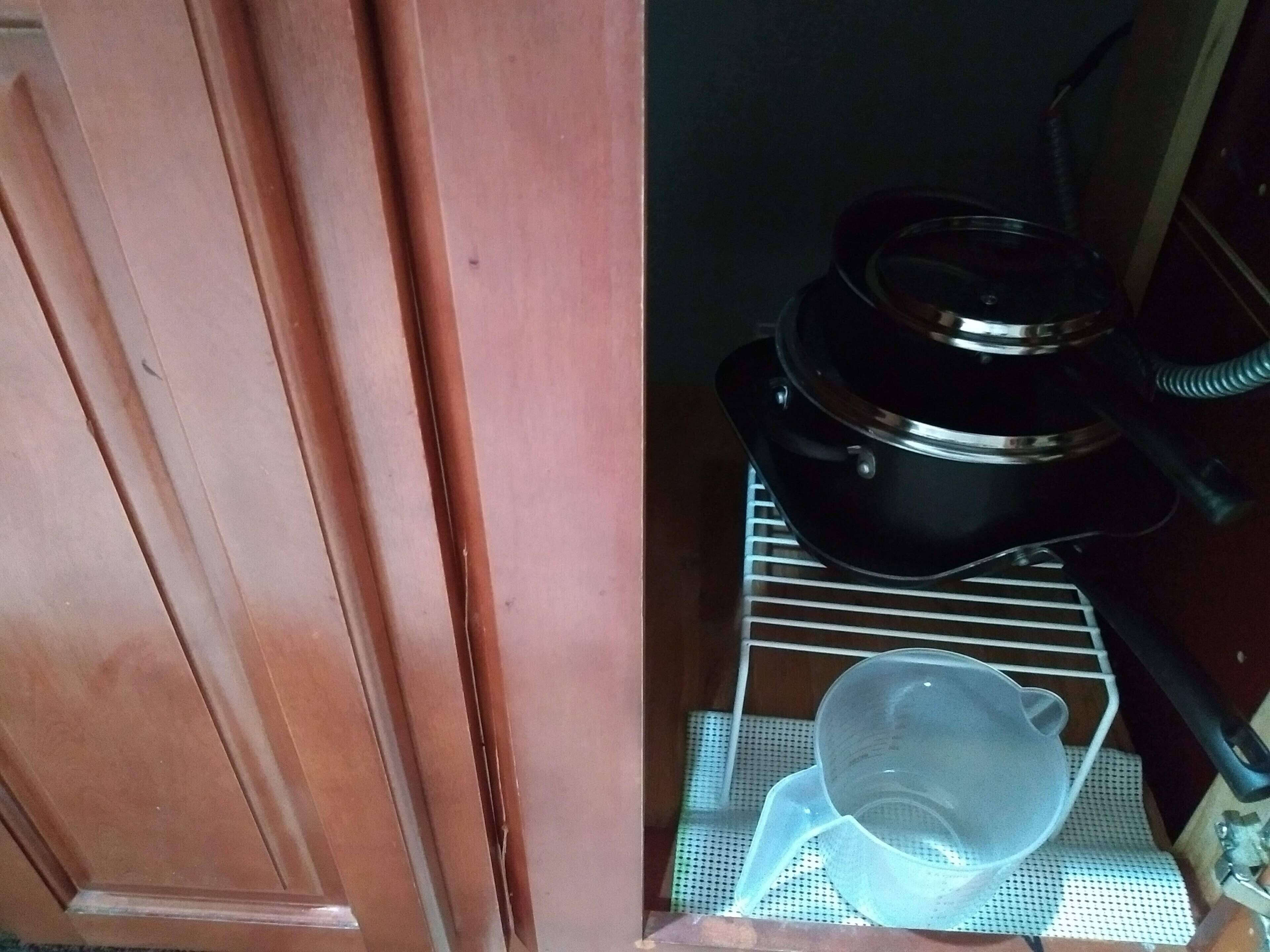 A kitchen area with a black appliance on a wire rack, a white plastic container, and a wooden door.