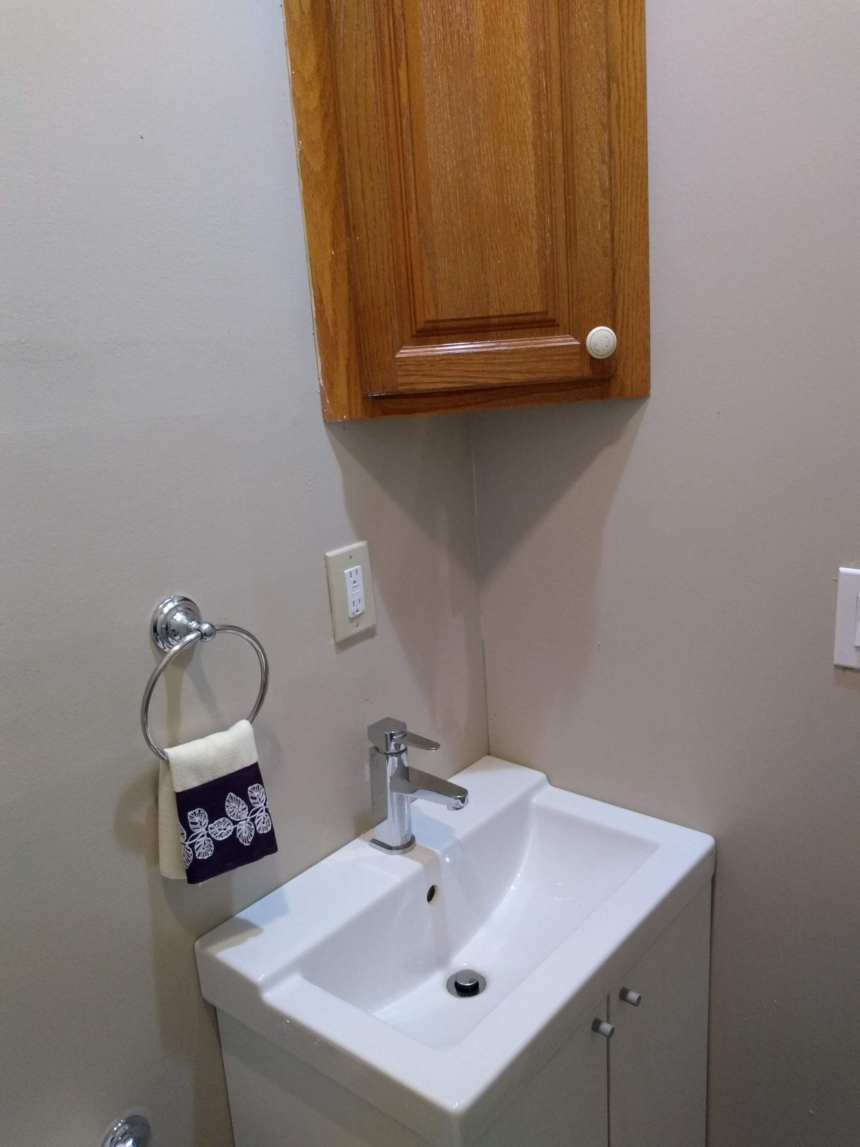 A bathroom with a white sink, a wooden cabinet above it, and a towel with a leaf pattern hanging on a metal ring.