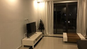 Uma sala de estar moderna com uma TV de tela plana em um suporte branco, uma pequena árvore de Natal e uma porta de vidro deslizante que dá para uma varanda.