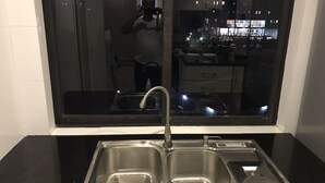 Cozinha moderna com pia de aço inoxidável, bancada preta e um espelho grande refletindo o interior.