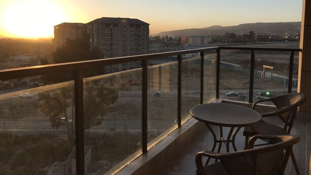 Uma varanda com vista para um pôr do sol, um edifício e uma estrada.