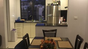 Uma área de refeições com mesa posta para quatro pessoas, rodeada por cadeiras, com vista para a cidade através de uma grande janela.