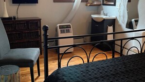 A bedroom with a bed, a TV, a dresser, a chair, a window, and a bathroom with a sink and mirror. - Heritage Classic Inn B&B - Room 3 (Hunter River)