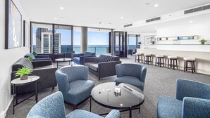 Un espace lounge moderne doté de sièges, d’un bar et offrant une vue sur la ville et la mer.