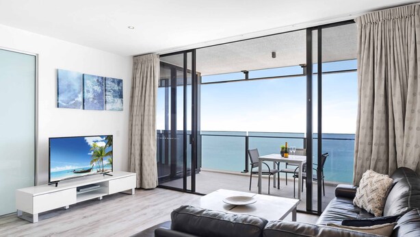 Un salon moderne doté d’un grand téléviseur, d’un canapé, d’une table basse et d’un balcon offrant une vue sur la mer.