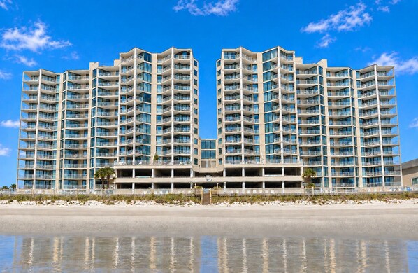 A high-rise hotel with multiple balconies and a reflective pool in front.
