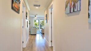 A hallway with a ceiling fan, recessed lighting, and a view into a living area with a sofa and a dining table.