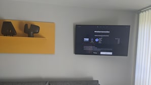 Una sala de estar moderna con un sofá gris, una pared de acento amarilla y un televisor de pantalla plana mostrando un mensaje de error de conexión inalámbrica.