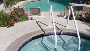 Una piscina con borde de azulejos, una escalera metálica y sillas de descanso.