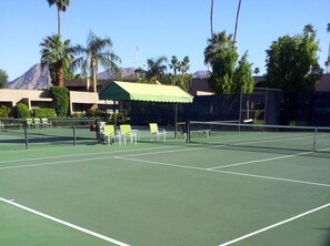 Ein Tennisplatz mit Netz, Stühlen und einer überdachten Sitzgelegenheit.