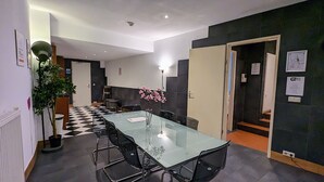Un salón de conferencias con una mesa de vidrio, sillas negras, una planta en maceta y un suelo a cuadros.