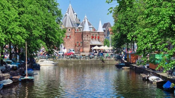 Un canal con barcos, un edificio de ladrillo rojo con múltiples torres y árboles a lo largo del canal.