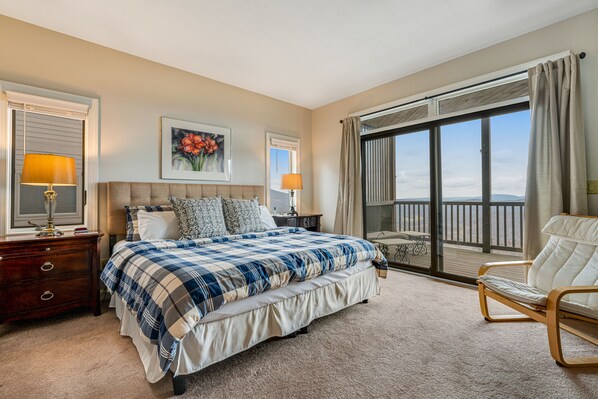 Une chambre avec un grand lit, deux tables de chevet avec des lampes, un fauteuil et un balcon avec vue.