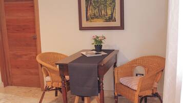Un comedor con mesa de madera, dos sillas de mimbre, un cuadro en la pared y una planta en maceta.