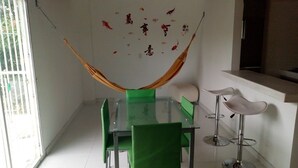 A dining area with a glass table, green chairs, a white chair, and a hammock. - apartamentos por dias el TUCAN (Santa marta)