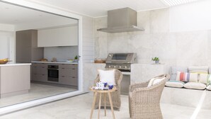A modern kitchen with a built-in oven and a stainless steel range hood. There is a wicker chair and a small table with a bowl and a cup. - Paddle on Seven Mile (LENNOX HEAD)