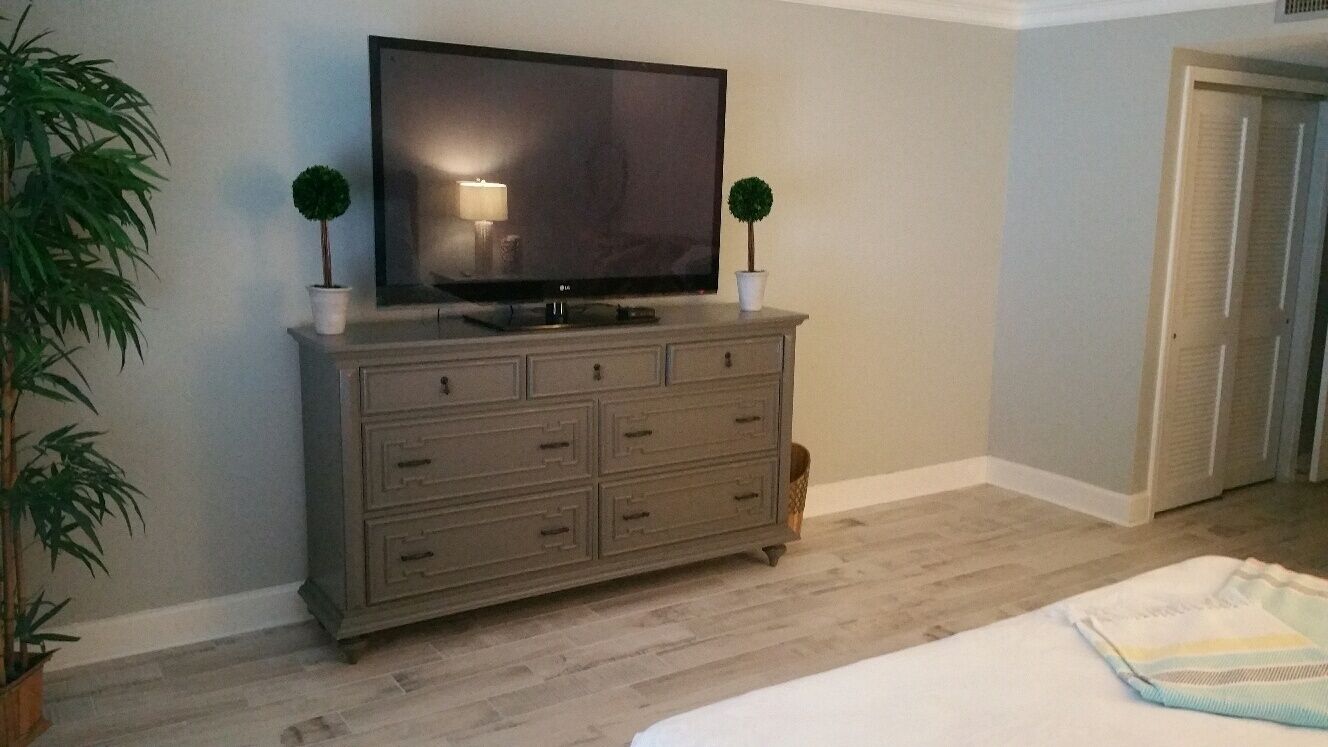 A bedroom with a bed, a dresser, a television, and two potted plants.