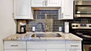 A kitchen with white cabinets, a stainless steel sink, a coffee maker, a microwave, and a stove.