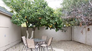 A patio with a round table and four chairs, surrounded by a white wall and a tree with fruit.