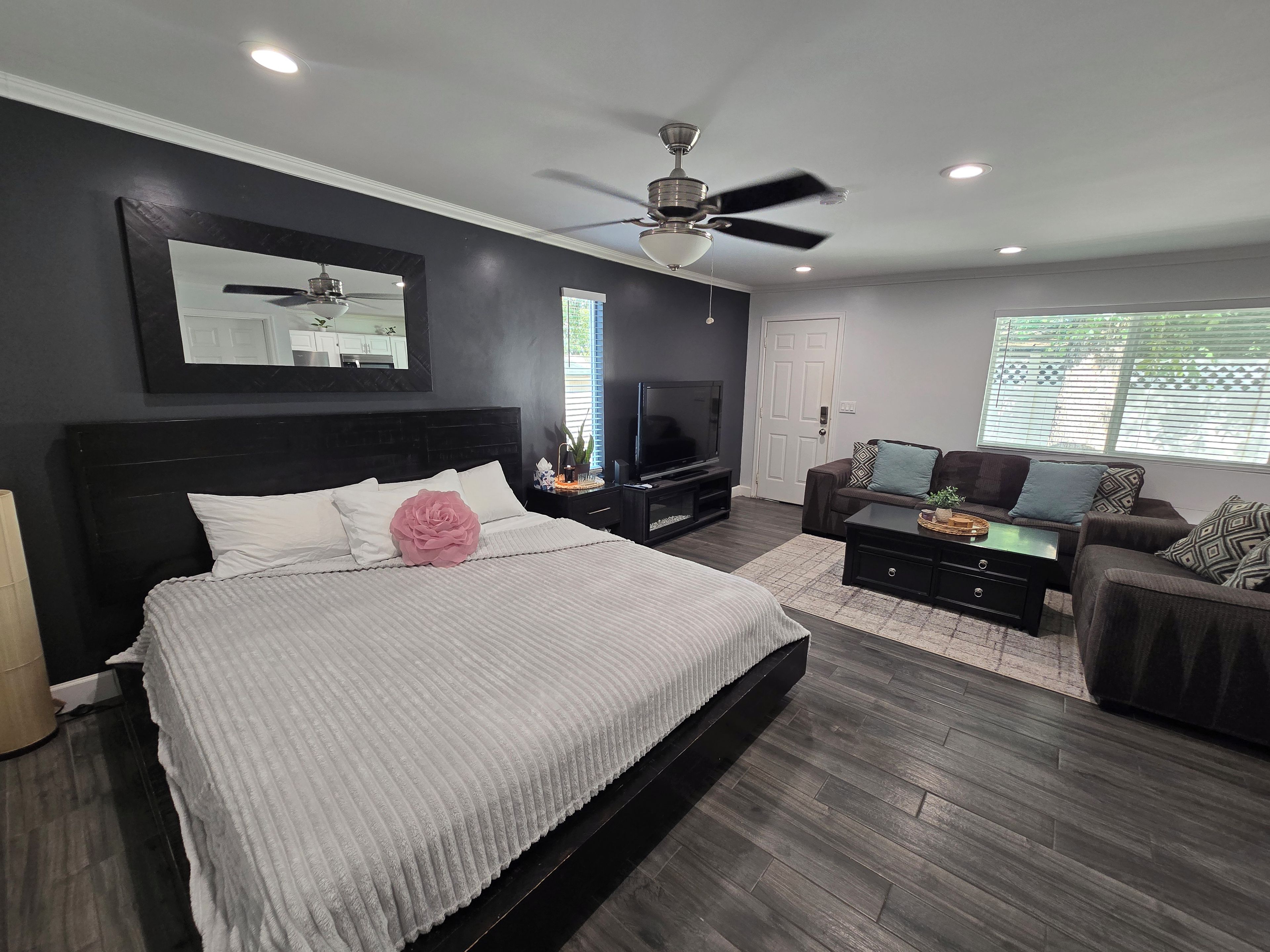 A modern bedroom with a large bed, a ceiling fan, a TV, and a seating area with a sofa and coffee table.