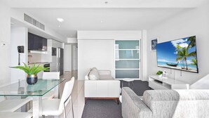 A modern living room with a glass dining table, white sofa, and a flat-screen TV on the wall. - H Residences Ocean View (Surfers Paradise)