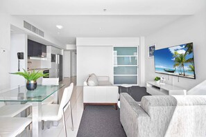 A modern living room with a glass dining table, white sofa, and a flat-screen TV on the wall. - H Residences Ocean View (Surfers Paradise)