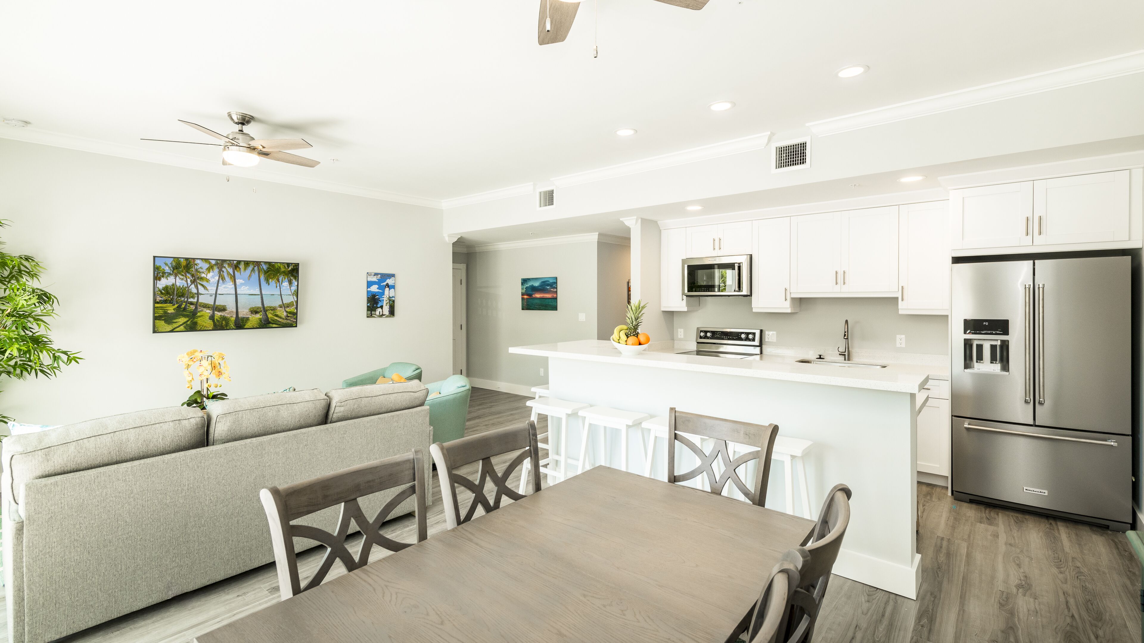A modern kitchen with white cabinets, a stainless steel refrigerator, and a dining area with a wooden table and chairs.