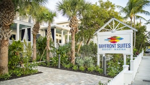 A sign for Bayfront Suites Resort Marina with a pathway lined with palm trees and a white fence.