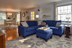 A living room with a blue sectional sofa, a coffee table, and a dining area with a table and chairs. - Beautiful Harbor Home with Ocean Views (Boothbay Harbor)