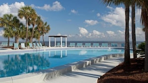 Zona de piscina con sillones de descanso y palmeras, con vista al océano.