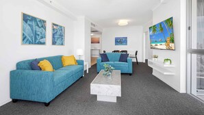 A modern living room with two teal sofas, a marble coffee table, and a painting of a beach scene. - Chevron Renaissance Ocean View (Surfers Paradise)