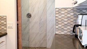 A modern kitchen with a glass shower enclosure, a coffee machine, and a patterned backsplash.