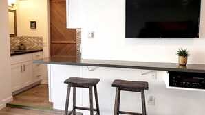 A modern kitchen with a flat-screen TV mounted above the counter, two stools, and a small plant on the counter.