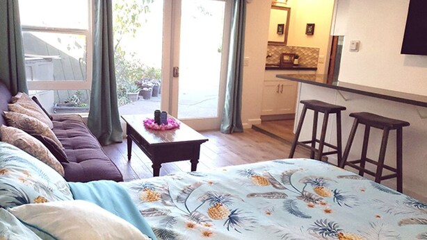 A bedroom with a bed, a sofa, a small table, and a kitchen area visible through an open door.
