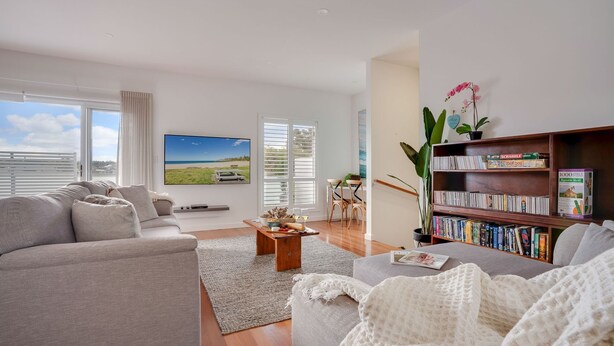 Una sala de estar moderna con un televisor de pantalla plana grande, una estantería y una zona de comedor con una mesa y sillas.
