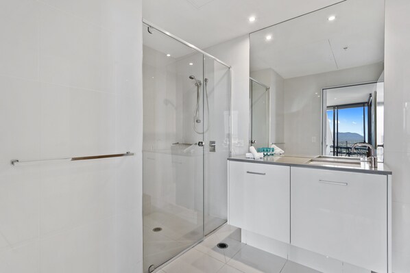 A modern bathroom with a glass-enclosed shower, a large mirror, and a view of the outdoors.