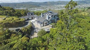 Ein großes Haus mit geräumiger Terrasse, umgeben von üppiger Vegetation und Bergen im Hintergrund.
