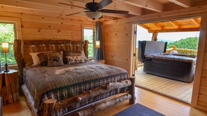 Une chambre dans une cabane en bois, avec un lit, un ventilateur de plafond et une vue sur l’extérieur.