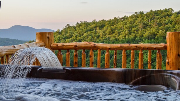 Un bain à remous doté d’une balustrade en bois et offrant une vue sur une colline boisée.