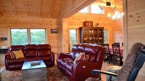 L’intérieur chaleureux d’un chalet en bois comprend des canapés en cuir, une table à manger avec des chaises et un lustre.