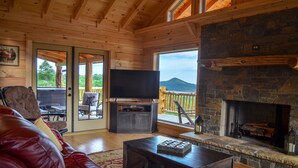 L’intérieur d’un chalet chaleureux, avec une cheminée en pierre, un téléviseur et un canapé en cuir rouge.