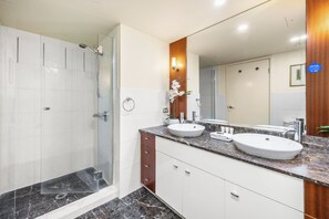 Un baño moderno con ducha envuelta en vidrio, dos lavamanos y un espejo grande.