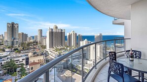 Ein Balkon mit Tisch und Stühlen, der auf eine Stadtansicht mit hohen Gebäuden und Blick auf das Meer blickt.