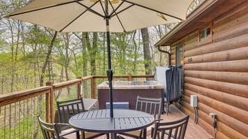 A wooden deck with a round table and chairs, a large umbrella, and a hot tub.