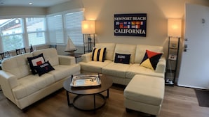 A living room with a beige sofa set, a coffee table, and a wall sign reading "Newport Beach California". -  Steps to Beach and Bay with Garage Parking (compact car) & Air Conditioning! (Newport Beach)