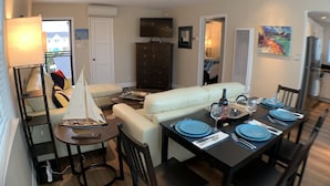 A dining area with a table set for four, a sofa, a small sailboat model, and a TV in the background. -  Steps to Beach and Bay with Garage Parking (compact car) & Air Conditioning! (Newport Beach)