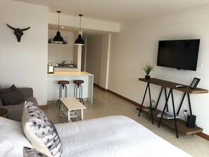 A modern living room with a sofa, a dining area with stools, a kitchen in the background, and a TV mounted on the wall. - Moderno Loft En El Corazon De Salta (Salta)